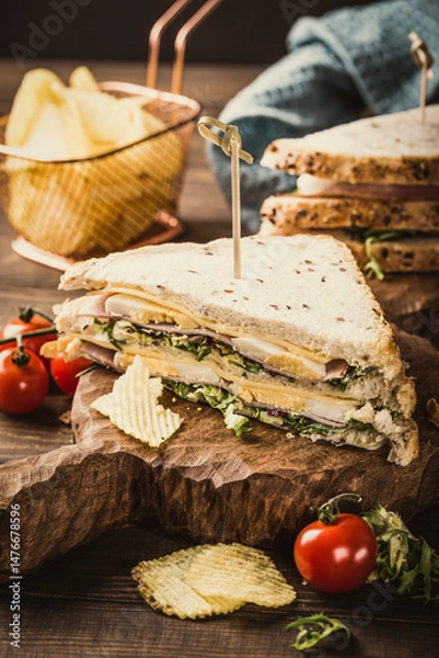 Fototapeta Stacked sandwich featuring fresh ingredients, served on a wooden board with crispy chips and cherry tomatoes, highlighting a delightful culinary experience
