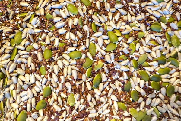 Fototapeta Assorted seeds including pumpkin, sunflower, and flax are scattered on a textured surface, showcasing natural colors and diverse shapes for healthy eating