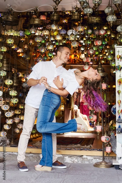 Obraz couple enjoys a playful dance in front of a lantern shop filled with colorful lights and decorations. atmosphere is lively, enhancing their joyful moment together in the marketplace