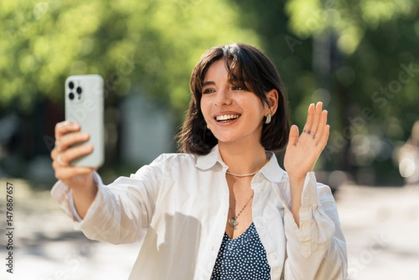 Fototapeta A selfie for the loved ones. Attractive woman with short hair student, chatting with her parents or friends from far away while on the move