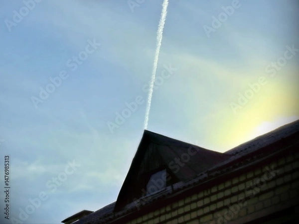 Fototapeta thin plane trail in blue sky above triangular roof, geometric shape in sunlight
