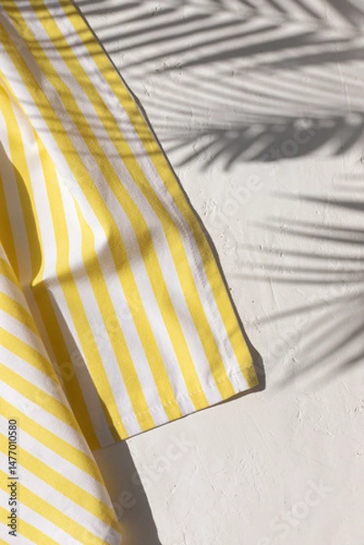 Obraz White plaster background with yellow striped pattern napkin or towel with tropical palm leaves shadows. Copy space	