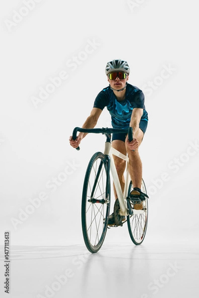 Fototapeta Full-length front view image of young man in full gear, cyclist in helmet and goggle riding bicycle isolated on white background. Concept of sport, competition, active lifestyle, endurance