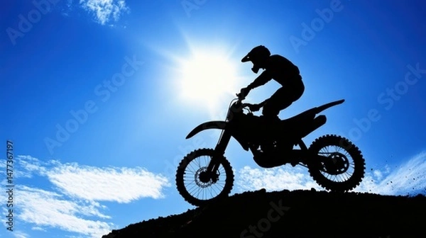 Fototapeta Silhouette of a Motocross Rider Performing a Jump Against a Bright Blue Sky with Sunlight Radiating and Clouds in the Background, Capturing Action and Adventure