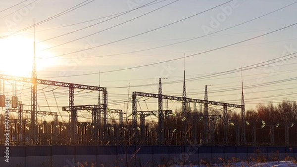 Obraz High voltage electrical insulators in power transmission substation against blue sky background; wires, cables, insulators at electrical power station, power grid infrastructure