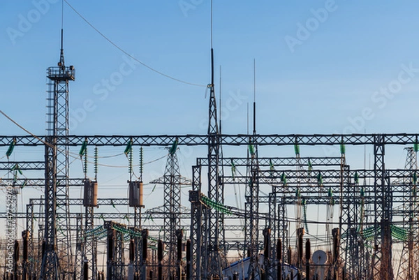 Obraz High voltage electrical insulators in power transmission substation against blue sky background; wires, cables, insulators at electrical power station, power grid infrastructure
