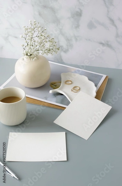 Fototapeta Blank paper sheet cards on home office desk workspace with coffee cup, vase, home decor on grey background. Wedding invitation cards. Flat lay, top view mockup with empty copy space.Life style concept
