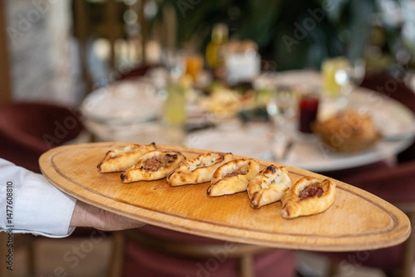 Fototapeta Close up view of a waiter holding baked, small portion Turkish pizza assortments with ground meat, cheese, and mixed on a wooden board in a restaurant.