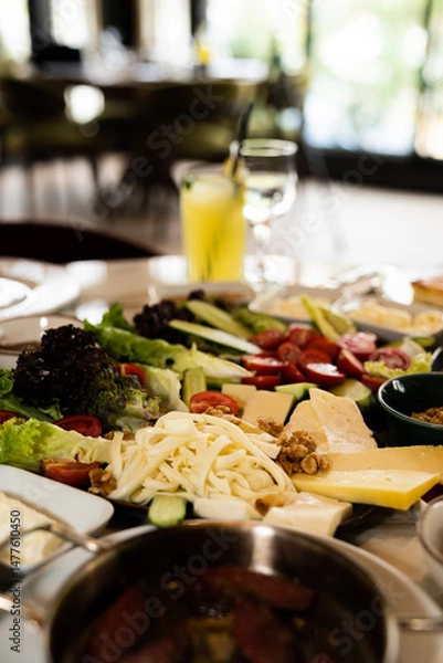 Fototapeta Close up view of a mix breakfast table with various foods, including cheese, lettuce, walnuts, tomatoes, cucumber, vegetables, and olives, in a restaurant.