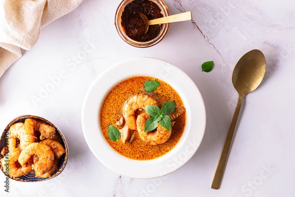 Obraz Fresh aromatic hot Thai soup Tom Yum with mushrooms, shrimps and different spices on white marble background top view. Tasty food concept.