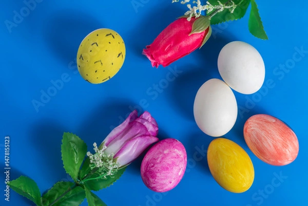 Fototapeta Colorful Easter eggs and artificial flowers on a vibrant blue background.