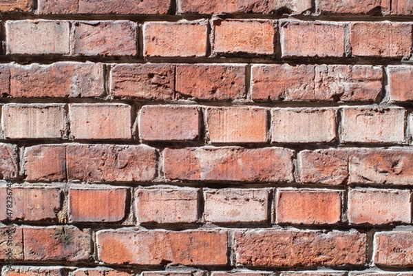 Fototapeta Dark brown brick wall in contrasting sunlight highlights its rough textured surface and chaotic masonry, old historical building,