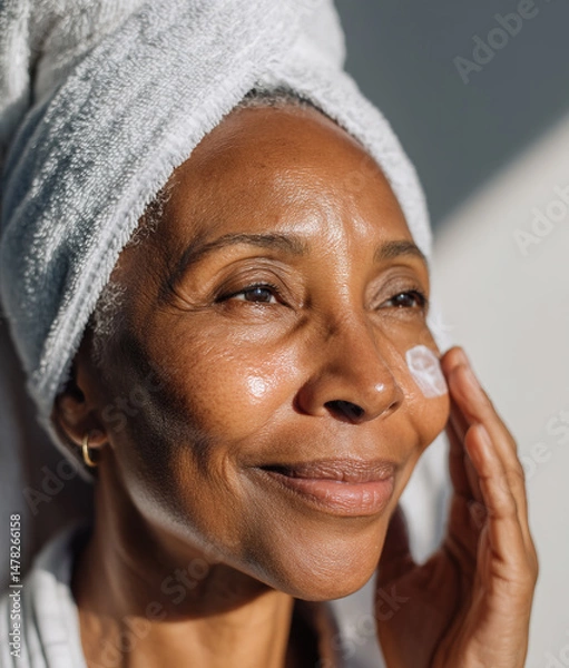 Obraz Smiling senior black woman applying moisturizing cream on face
