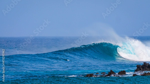 Fototapeta Perfect glassy wave curls and breaks gracefully near a jagged volcanic shoreline. Turquoise ocean glistens and creates a surfable wave framed by rocky outcrops of the coastline at Canary Islands.