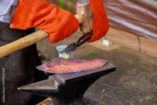 Obraz Craftsman expertly hammering heated metal on an anvil while showcasing traditional blacksmithing during axe making