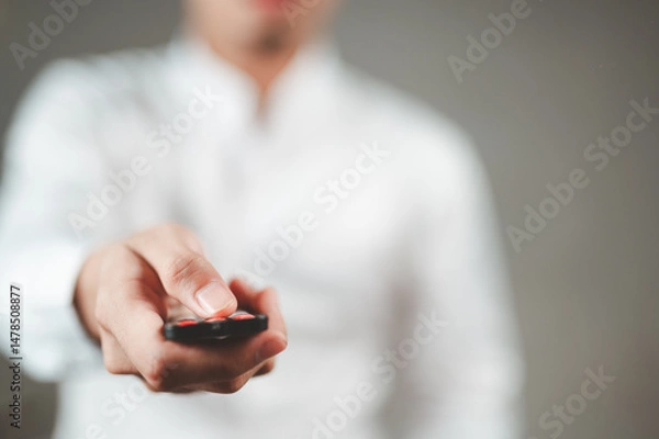 Fototapeta A businessman in a white shirt is pressing a remote control, pointing it at your face.