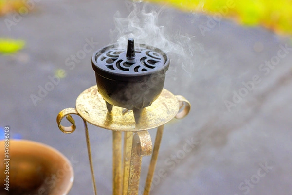 Obraz Incense sits on decorative incense holder as smoke rises, creating serene atmosphere in an outdoor space