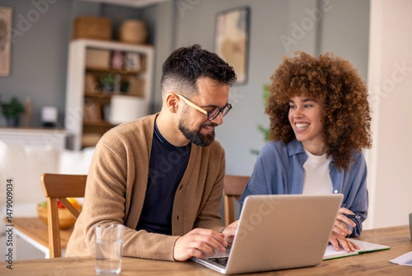Fototapeta Mid-Aged Diverse Couple Collaborating On Project Using Laptop In Cozy Home Office With Natural Light