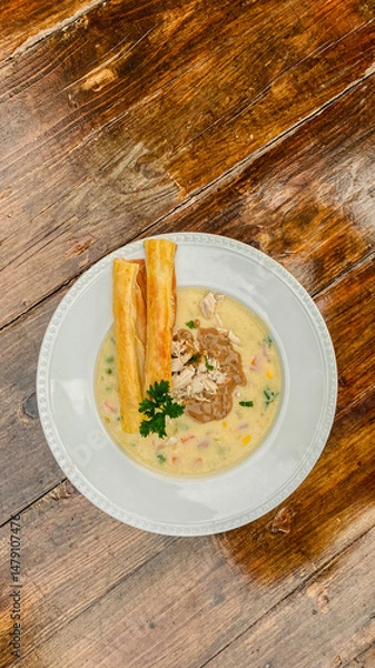 Fototapeta A delightful creamy soup with vibrant herb garnish, paired with a crunchy breadstick on a beautifully textured wooden table.