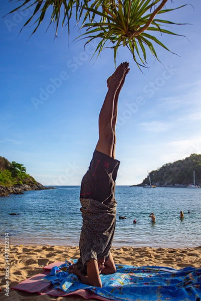 Obraz A man doing yoga in a headstand pose by the sea. Yanui Beach is a small, quiet beach with a small island in front of the clear blue water. It is a great place for snorkeling and relaxing.
