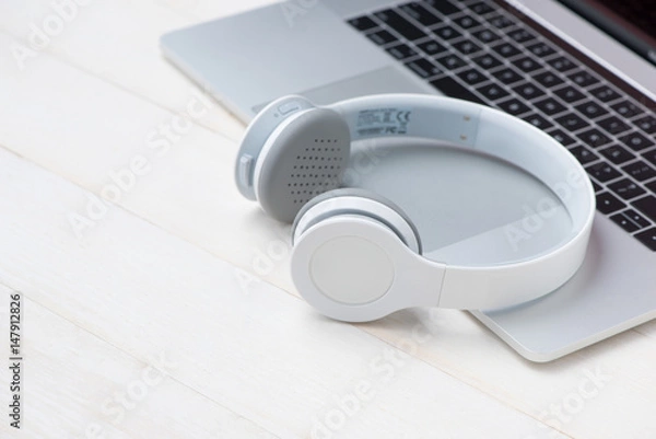 Fototapeta Laptop computer on white table with headphone and coffee cup. View from above