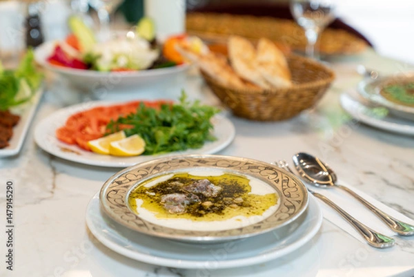 Fototapeta Traditional Turkish cuisine nesting soup served on white table. Lamb meat, chickpea and rice meatballs in lamb broth thickened with yoghurt, flour and egg; All served with mint oil.
