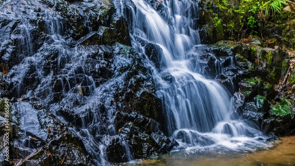 Fototapeta Tropical Waterfall Cascading Over Rocks in Lush Green Forest