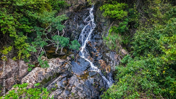 Fototapeta Beautiful Small Waterfall Surrounded by Lush Green Foliage and Natural Rock Formations