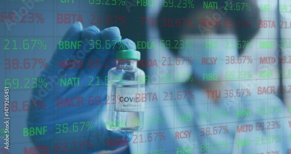 Fototapeta Researcher wearing mask and gloves examining vial labeled in research lab, with stock ticker