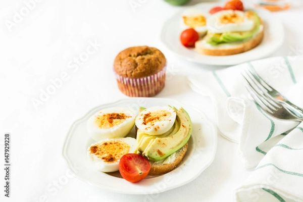 Fototapeta Healthy breakfast: toasts with avocado slices, tomato, paprika and eggs on white tableware. Selective focus