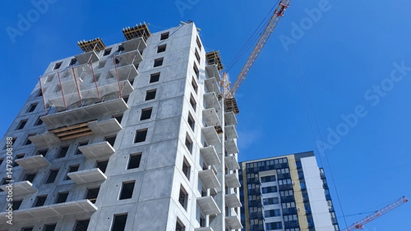 Obraz Construction crane against the background of a concrete slab house under construction. Construction of an apartment building.