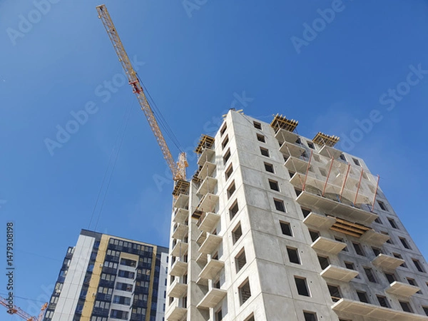Obraz Construction crane against the background of a concrete slab house under construction. Construction of an apartment building.