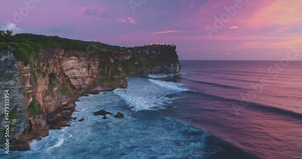 Fototapeta Uluwatu Temple standing on high cliff overlooking the beautiful Pantai Dreamland Beach with colorful sky during sunset in Bali, Indonesia, creating stunning scenery