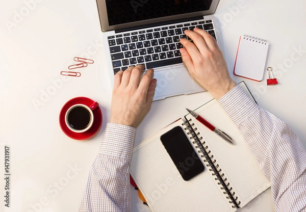 Obraz A man writes a pen in a notebook, to work in the office, laptop on a white table, a red mug of coffee.