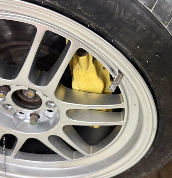 Obraz Detailed look at a yellow brake caliper nestled within an alloy wheel, highlighting automotive design features and performance enhancement.