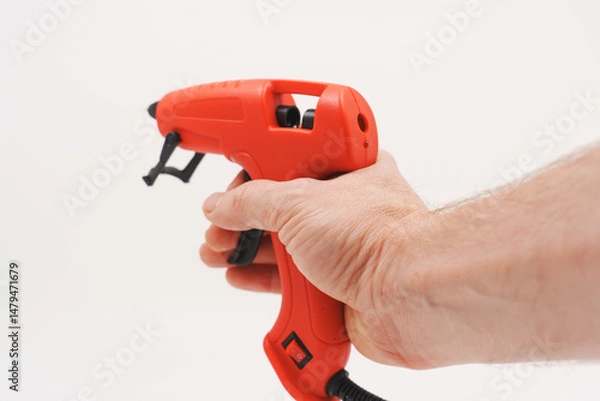 Obraz A red glue gun with a black wire in hand on a white background.