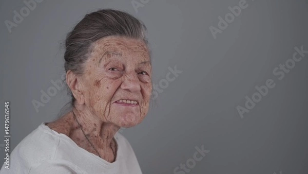 Fototapeta Senior woman 90 years old smiles, laughs and shows a denture on a gray background. Elderly female with deep wrinkles and gray hair happy in a good mood studio portrait looking at camera.