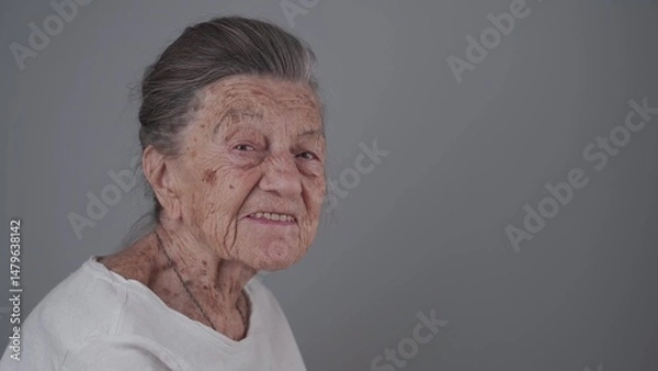 Fototapeta Senior woman 90 years old smiles, laughs and shows a denture on a gray background. Elderly female with deep wrinkles and gray hair happy in a good mood studio portrait looking at camera.