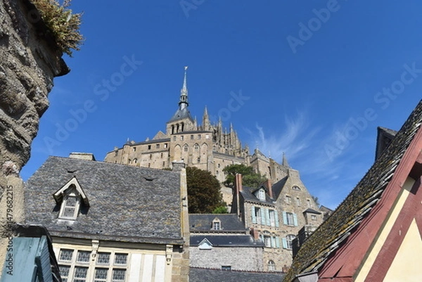 Obraz Vue en contre-plongée de l'abbaye du Mont Saint-Michel, derrière les vieux bâtiments à son pied, sous un beau ciel bleu