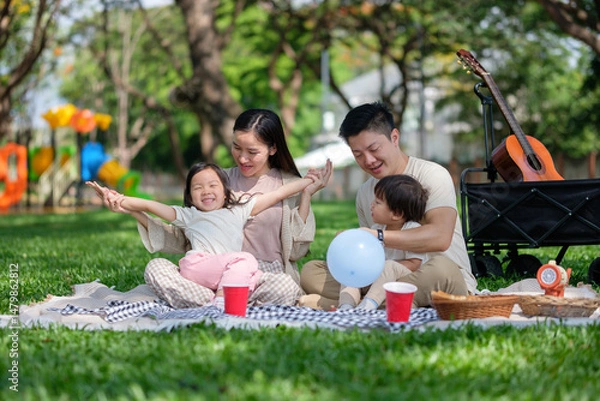Fototapeta Joyful family enjoying picnic time at the park with kids playing and parents relaxing together.