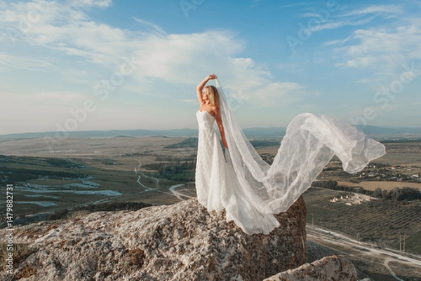 Obraz a woman in a white dress, a bride on a mountain with a blue sky. Beautiful nature, freedom, enjoyment of life. High quality photo