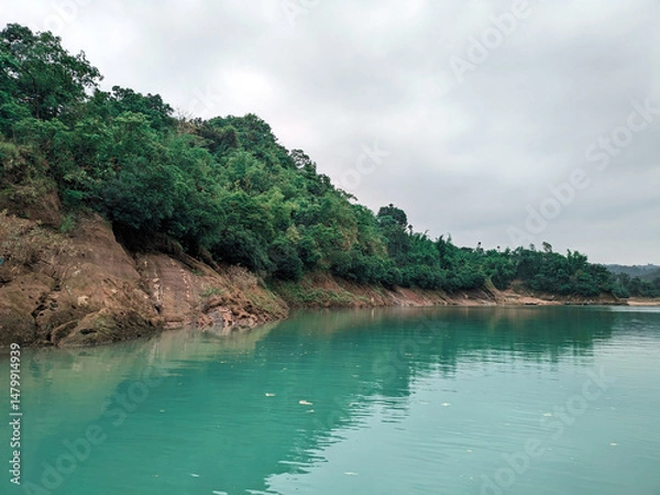 Fototapeta Serene river with clear blue water bordered by lush forest and rocky cliffs