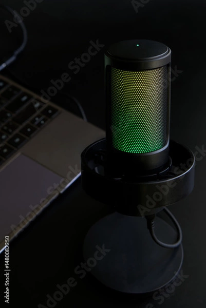 Fototapeta Close-up of a stylish RGB microphone beside a laptop, ideal for promoting streaming, gaming, or podcast equipment. Photo, selective focus