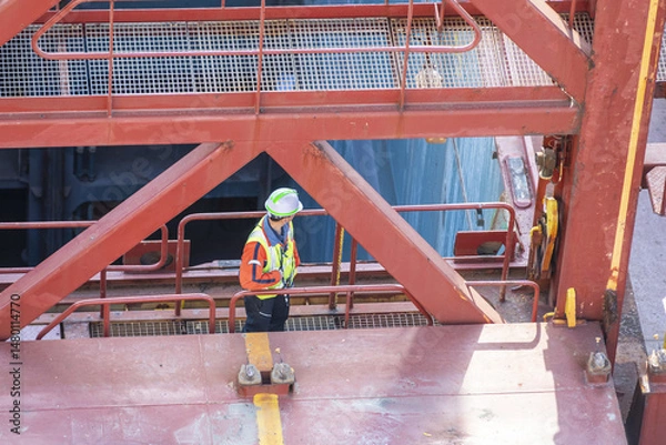 Fototapeta A port employee, stevedore, standing on deck of a container ship during his daily routine activities on board of merchant vessel.
