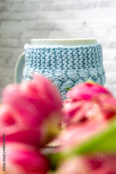 Fototapeta Pink tulips blurred foreground, open book and a mug of freshly brewed coffee or tea. Spring set