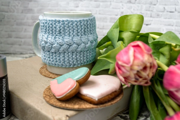Fototapeta Pink tulips blurred foreground, open book and a mug of freshly brewed coffee or tea. Spring set