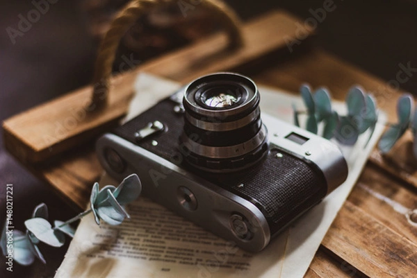 Fototapeta Retro camera on old book and eucalyptus branch on wooden background, flat lay. Vintage style