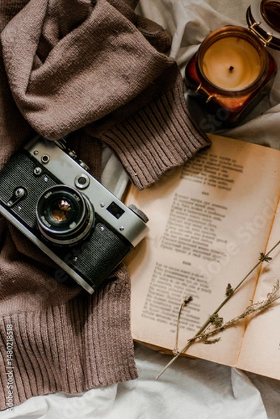 Fototapeta Vintage film camera with an old book wrapped in a warm knitted sweater and an extinguished candle next to it. View from above on a flat surface.
