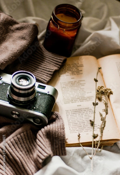 Fototapeta Vintage film camera with an old book wrapped in a warm knitted sweater and an extinguished candle next to it. View from above on a flat surface.