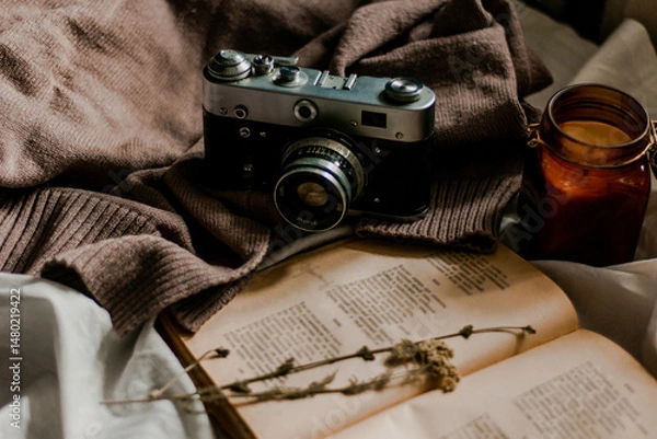 Fototapeta Vintage film camera with an old book wrapped in a warm knitted sweater and an extinguished candle next to it. View from above on a flat surface.